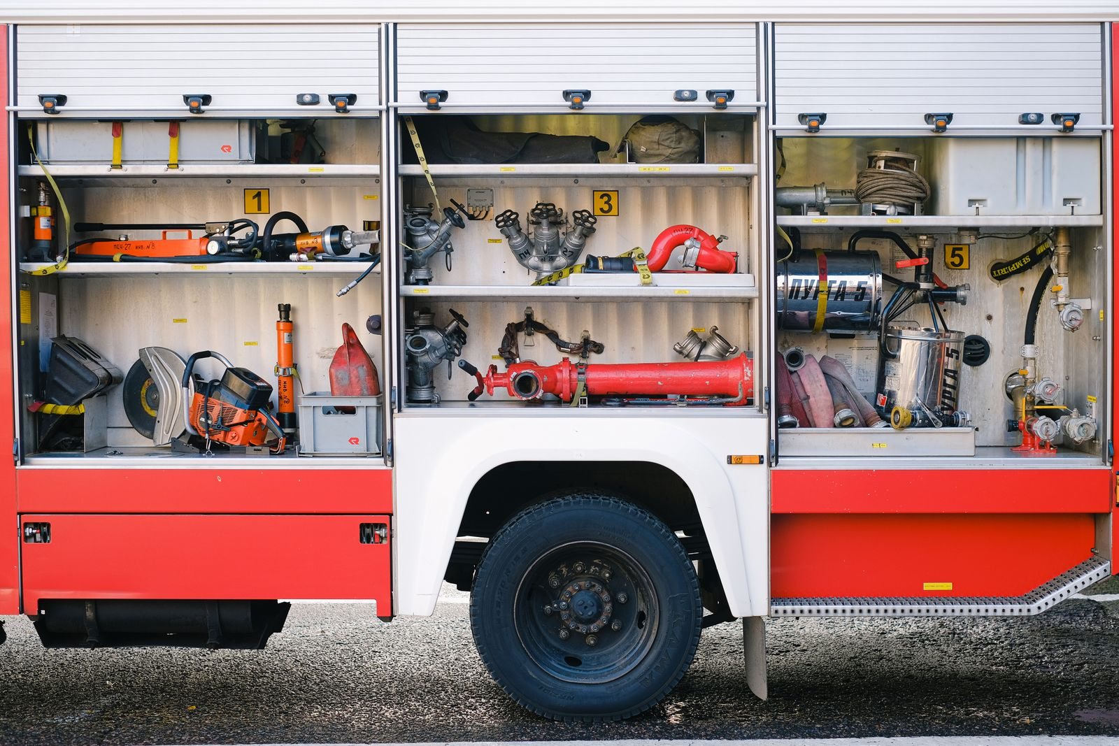 Organized firefighting tools in the open compartments of a red fire engine.